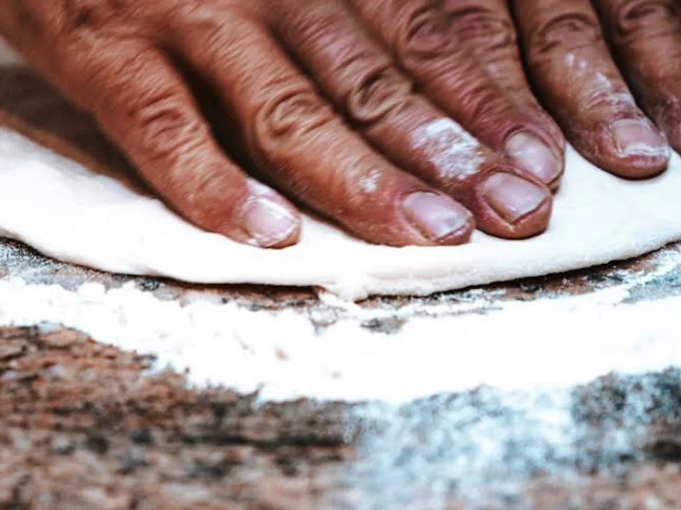 Le mani del pizzaiolo stendono l'impasto sulla farina
